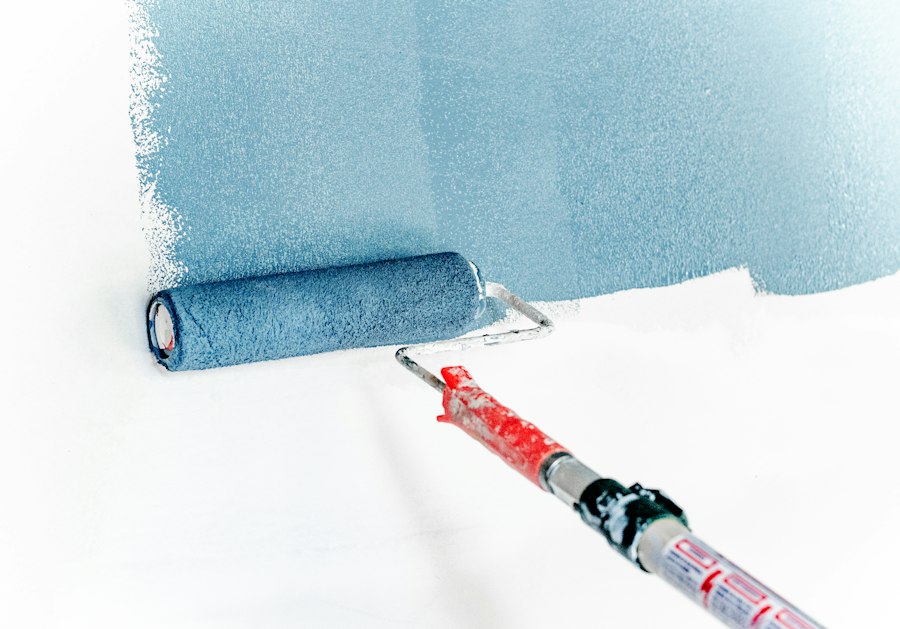 Rullo che applica pittura azzurra su parete bianca